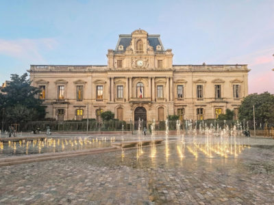 Fontaine sèche linéaire avec jets lumineux intégrée à une place patrimoniale devant un bâtiment institutionnel